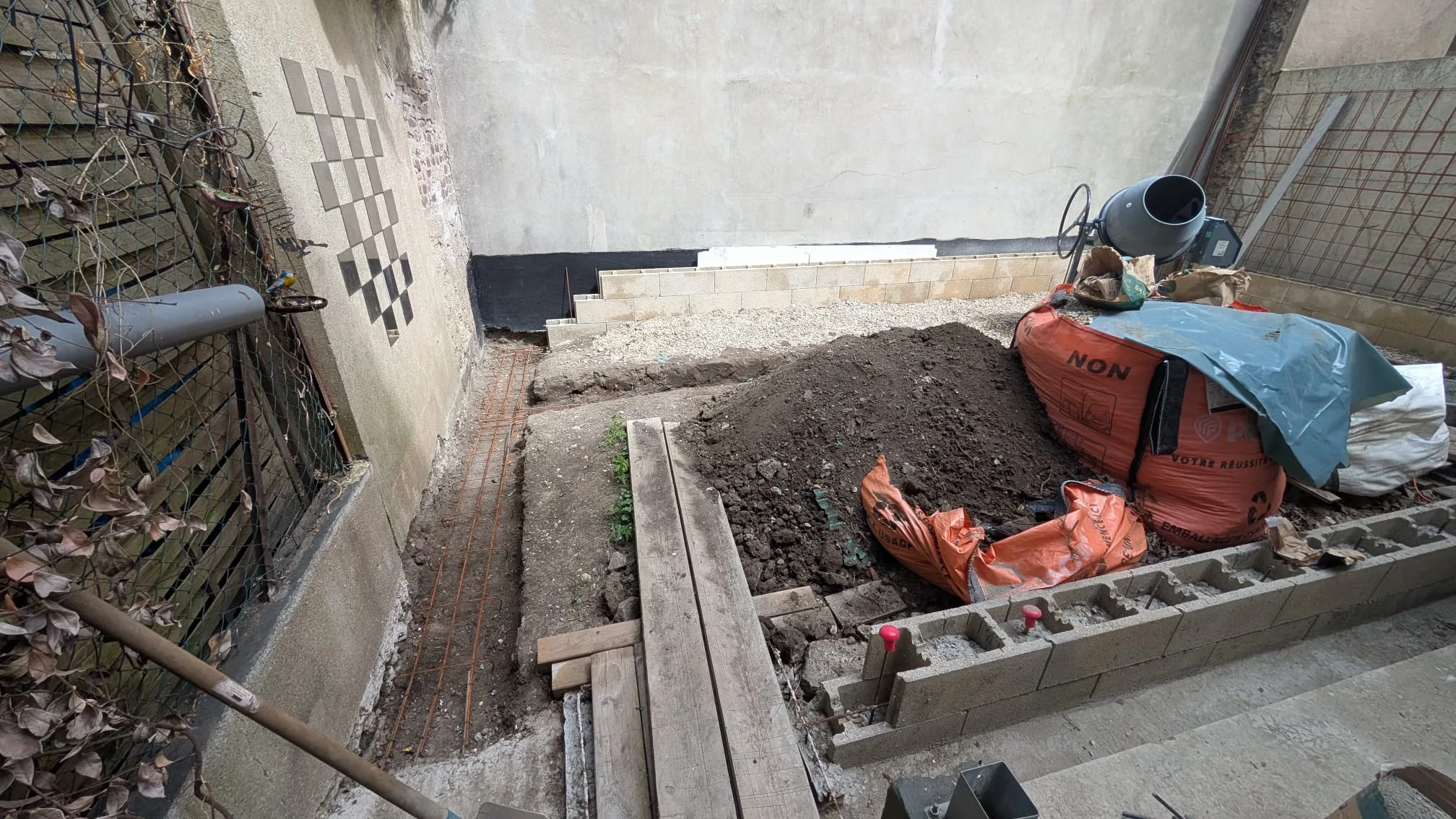 Fouille des fondations avec premier alignement et sac de béton, le long du mur de la cour