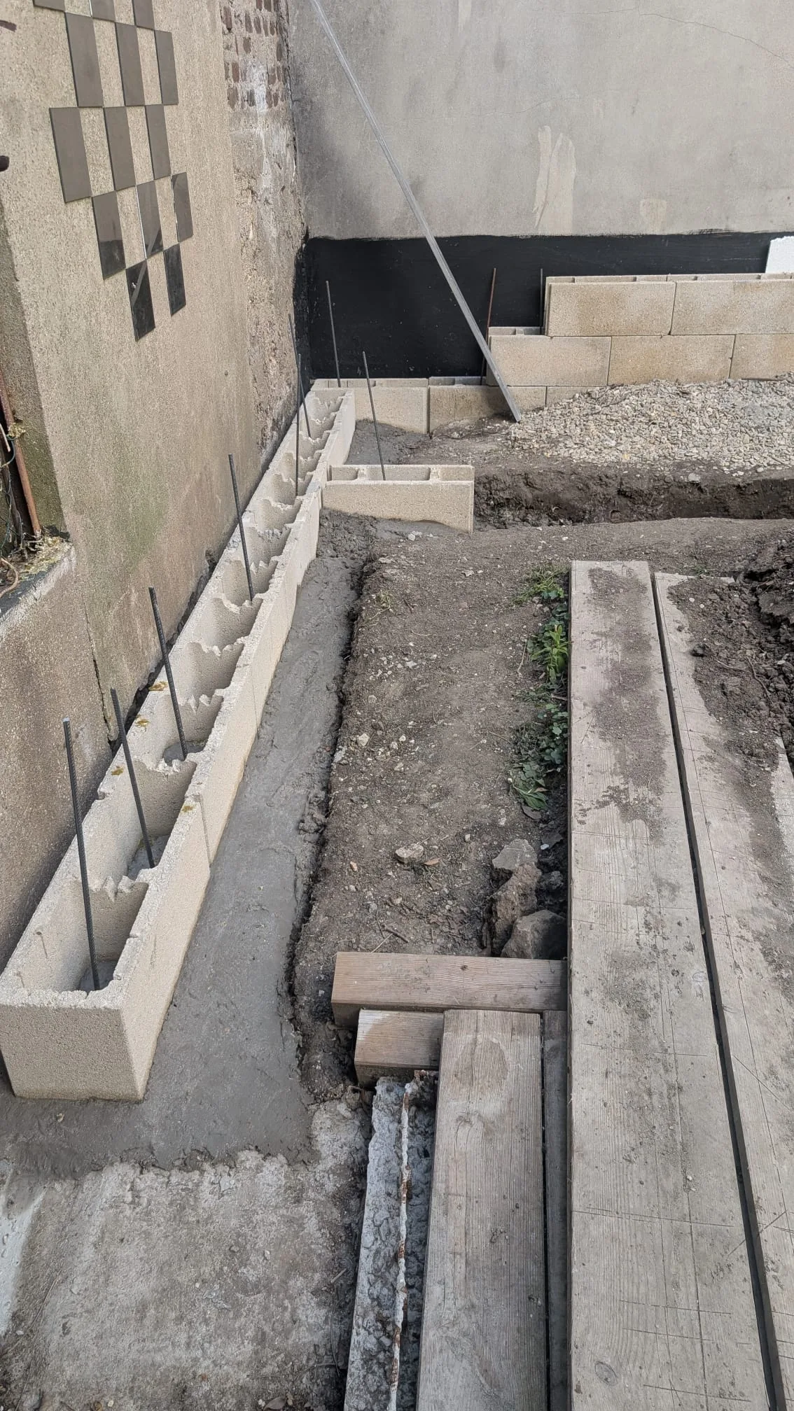 Premières rangées de parpaings montées le long du mur avec les fers verticaux en attente