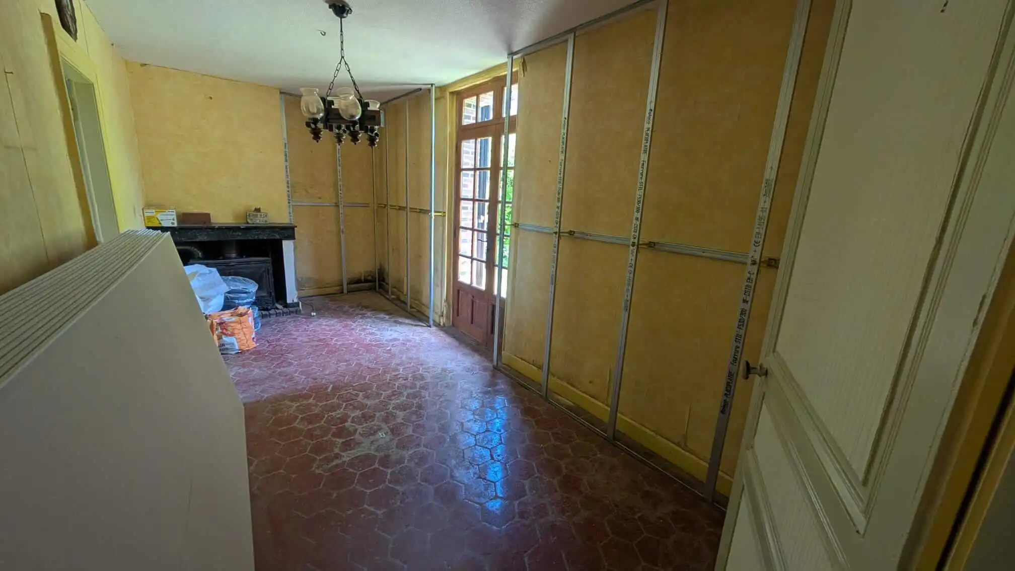 Longue pièce avec ossature Optima posée sur toute la périphérie, cheminée et chandelier visibles