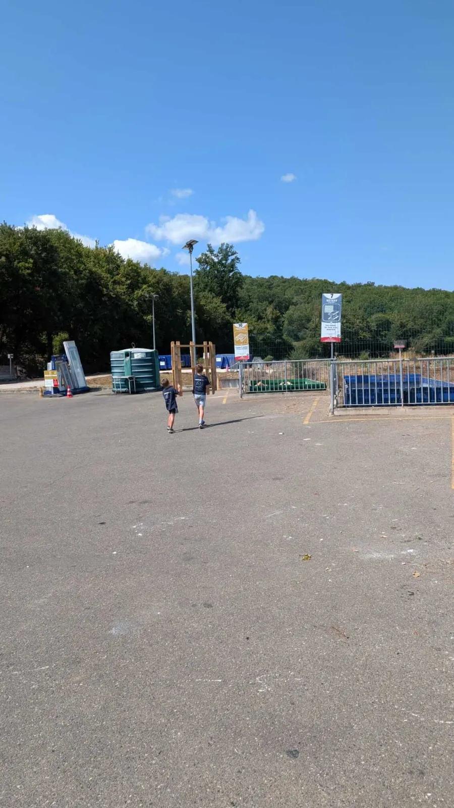 Les deux enfants portent ensemble un chargement de bois vers la benne de la déchetterie