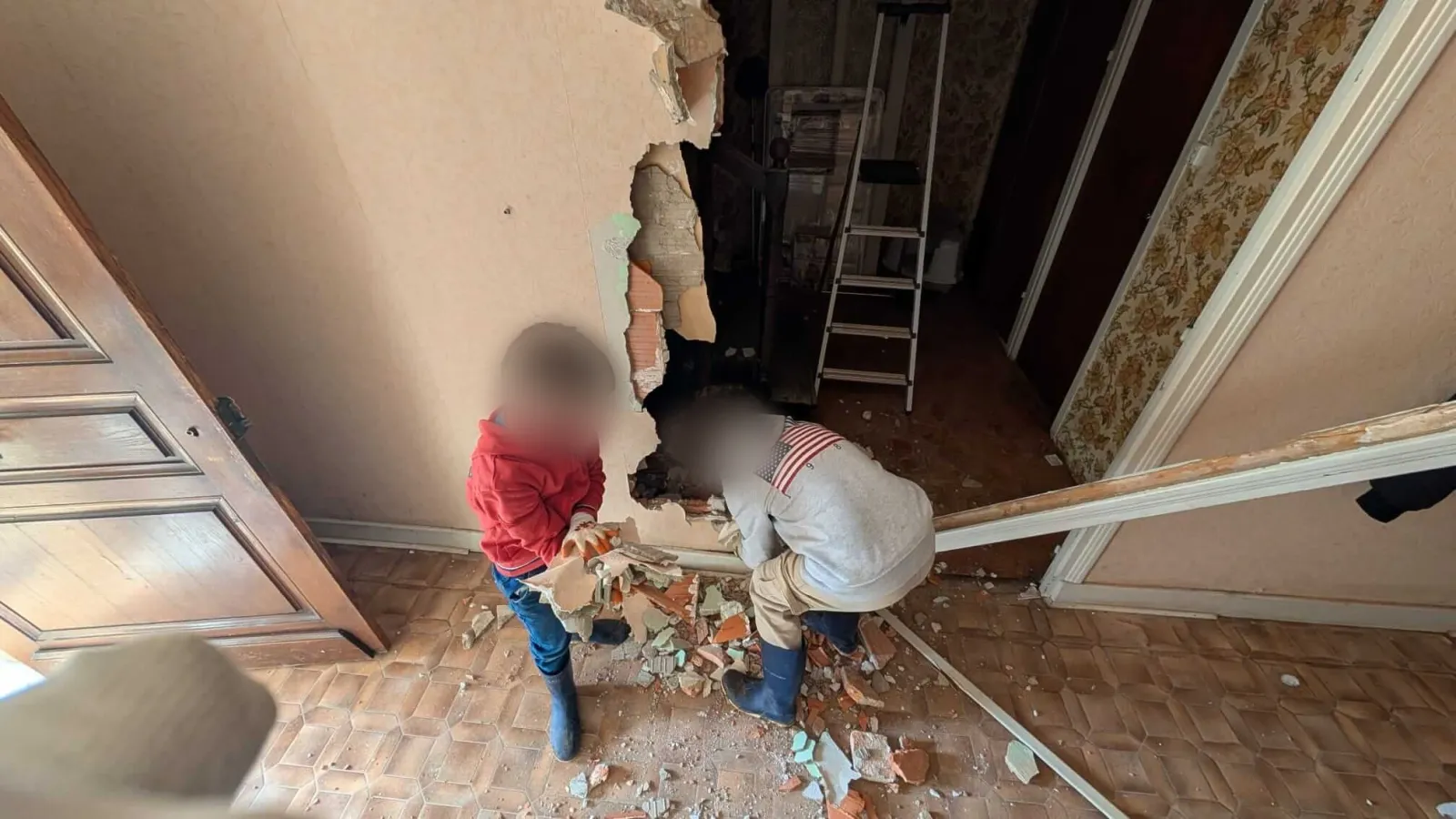 Les deux enfants ramassent les gravats au pied d'une cloison démolie du rez-de-chaussée
